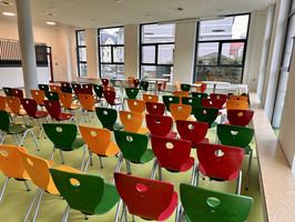 Foto mit Blick von hinten auf die bunten Stühle, die in der Aula in Reihen aufgestellt sind.