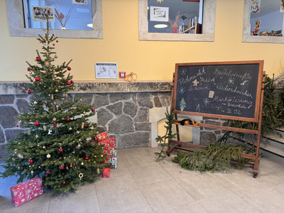 Foto vom Weihnachtsbaum in der Aula direkt im Eingangsbereich mit Tafel zur Begrüßung und Geschenken unter dem Baum.