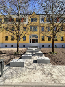 Blick auf den ehemaligen Haupteingang, der im Zuge der Komplettsanierung zu einem Deko-Fenster umfunktioniert wurde. Davor stehen Sitzgelegenheiten.