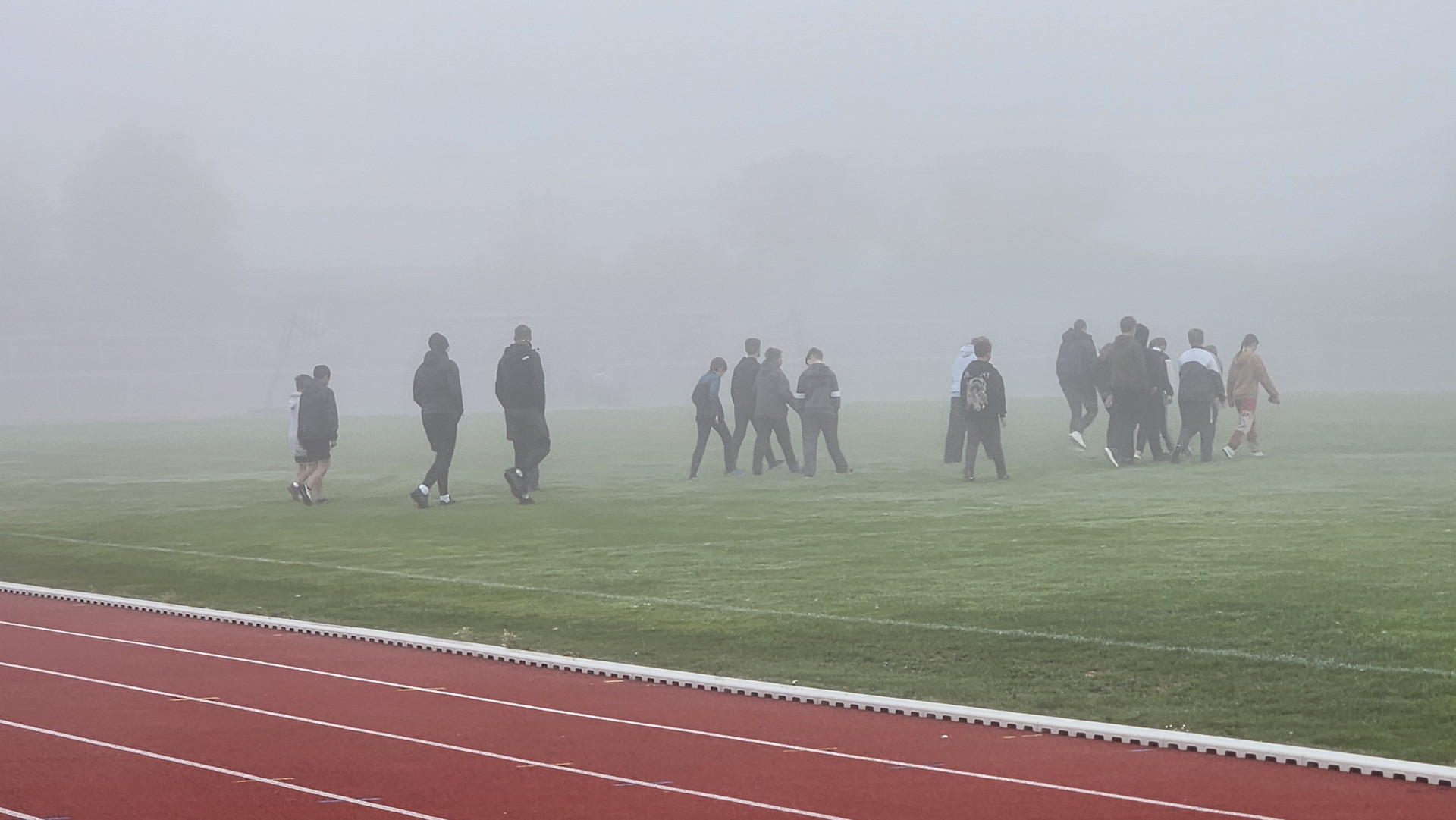 Sportler gehen auf das Spielfeld des Stadions im dichten Nebel.