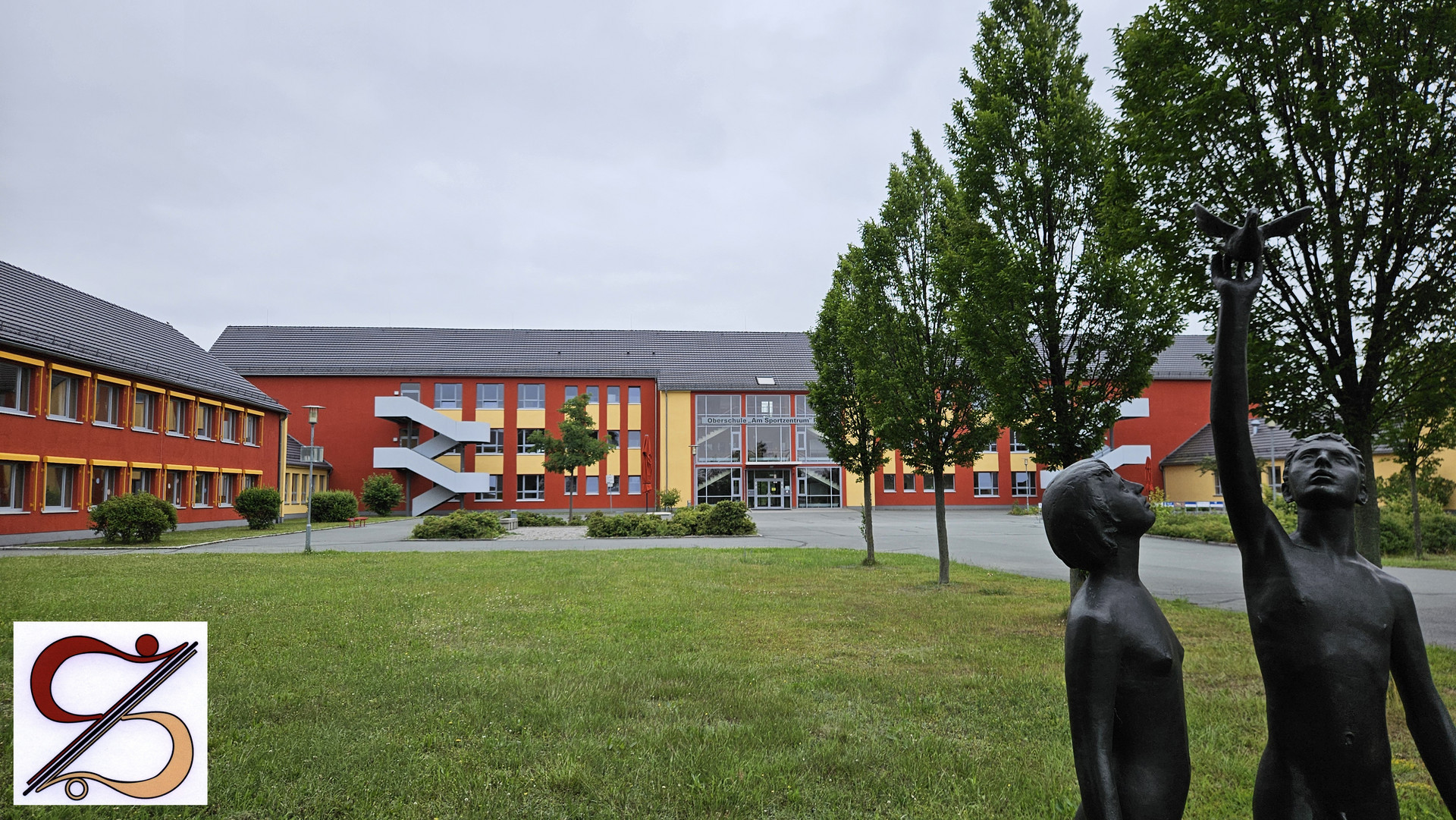 Blick auf das Schulgebäude mit der Plastik im Vordergrund